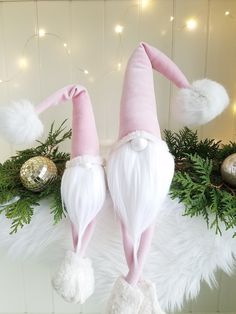 two white and pink gnomes are sitting next to christmas decorations