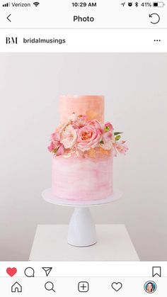 a three tiered cake with pink frosting and fresh flowers on top, sitting on a white pedestal