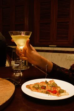 a person holding a wine glass with a slice of pizza on the plate next to it