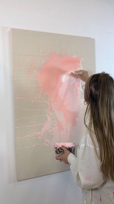 a woman is painting on the wall with pink paint