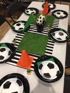 a soccer themed table setting with black and white plates, orange napkins, and green grass