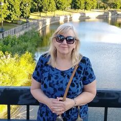 a woman wearing sunglasses standing next to a lake