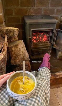 a person sitting in front of a fire holding a bowl of soup