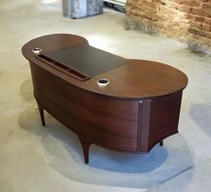 a wooden desk sitting on top of a white floor next to a brick wall in an empty room