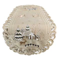 an embroidered christmas ornament is shown on a white cloth covered tablecloth with a house and trees in the background