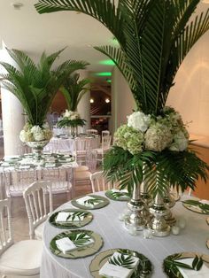 the table is set with white and green plates, silver vases, and palm leaves