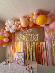 balloons and streamers are hanging from the ceiling above a table at a first birthday party