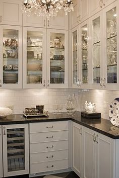 a kitchen filled with lots of white cabinets and black counter top space under a chandelier