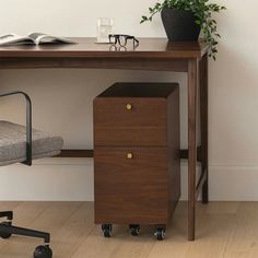 a wooden desk with two drawers and a chair next to it on casteors in front of a white wall