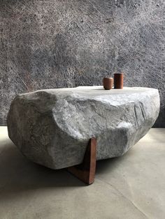 a stone table with two cups on it in front of a gray wall and concrete floor