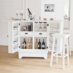 an open cabinet with wine bottles and glasses in it on the floor next to two stools