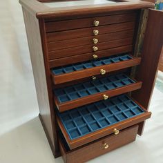 a wooden jewelry box with three drawers and blue trays on it's sides