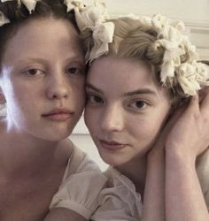 two women with flower crowns on their heads are posing for the camera, both wearing white dresses