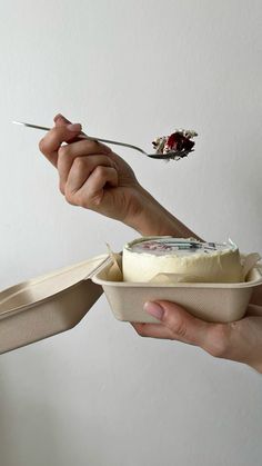 a person holding a fork and eating something out of a paper container with cheese in it