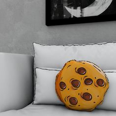 a yellow cookie pillow sitting on top of a white couch next to a black and white painting