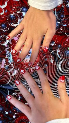 two hands touching each other with red and black designs on them in front of an abstract background