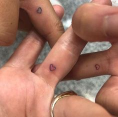 two people holding hands with hearts on their fingers and one has a small heart tattoo on the middle finger