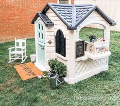 a small white dog house sitting on top of a lush green field next to a brick building