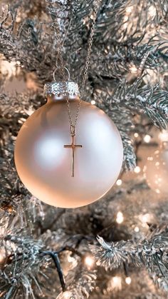 a white ornament with a cross hanging from it's side on a christmas tree