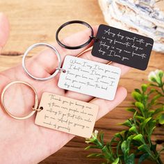 a person holding three different key chains with writing on one end and two small tags attached to the other