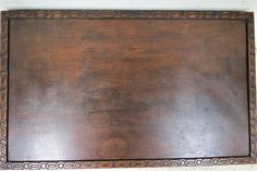 an old wooden board with intricate designs on it's edges and sides, sitting against a white wall