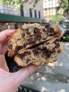 a hand holding a chocolate chip cookie in front of a building on a city street