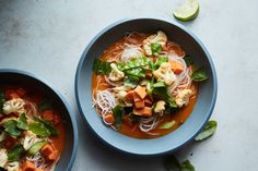 two bowls of soup with noodles, carrots and spinach on a white table