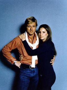 a man and woman standing next to each other in front of a blue wall with their arms around each other