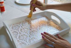 two hands are using a paintbrush to decorate a decorative tray