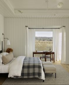 a bedroom with a bed, desk and chair in front of a large open window