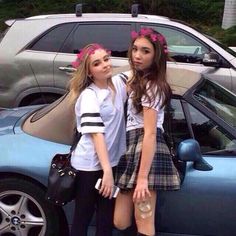 two girls standing next to each other in front of a car