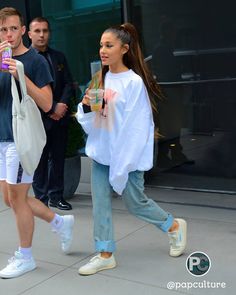 two people are walking down the street while one holds a cell phone in her hand