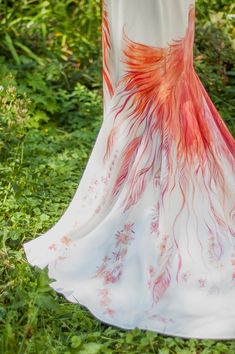 a woman in a white dress with red feathers on it's back, walking through the grass