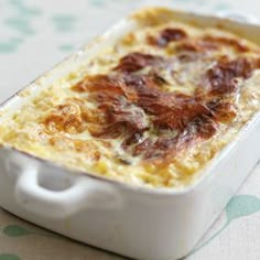 a casserole dish with meat and cheese in it sitting on a tablecloth