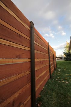 a wooden fence in front of a house with grass on the ground and trees behind it