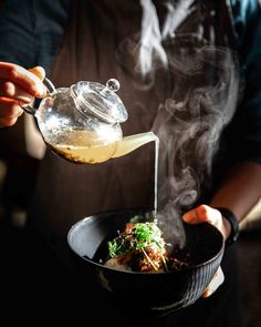 a person pouring something into a bowl with steam coming out of it and on top of some food