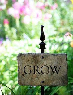 a sign that says grow on it in front of some flowers