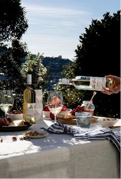 a person pouring wine into a glass at a table with food and fruit on it