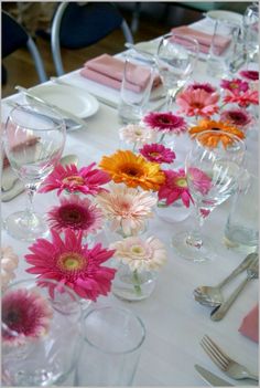 the table is set with pink, orange and yellow flowers in glass vases on each side