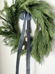 a christmas wreath hanging on the wall with a ribbon and bells attached to it's front door