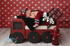 a baby sleeping on top of a toy fire truck with stuffed animals next to it