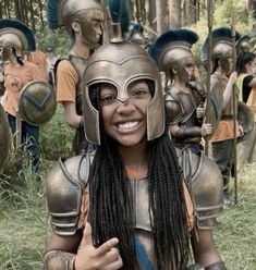 a woman with dreadlocks is posing in front of some spartan helmets and holding her thumb up