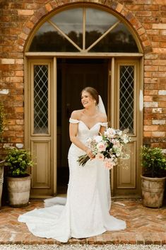 a bride standing in front of a brick building holding her bouquet and smiling at the camera