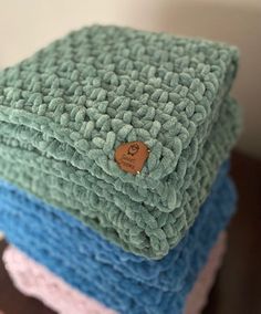 three blankets stacked on top of each other with a wooden button in the middle one is blue, green and pink