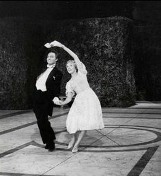 an old black and white photo of two people dancing in the middle of a courtyard