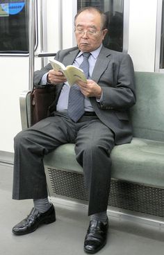 a man in a suit and tie sitting on a subway train reading a paper while holding a briefcase