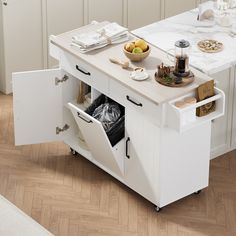 a white kitchen island with an open trash can underneath it and other items on the counter