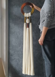 a woman is holding a wooden and white wall hanging with tassels on it