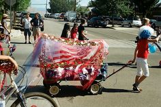 a woman pushing a red wagon with an american flag covering it's sides on a city street