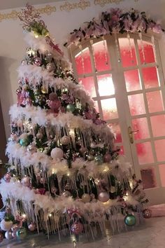 a white christmas tree decorated with pink and green ornaments, hanging from a ceiling in front of a door